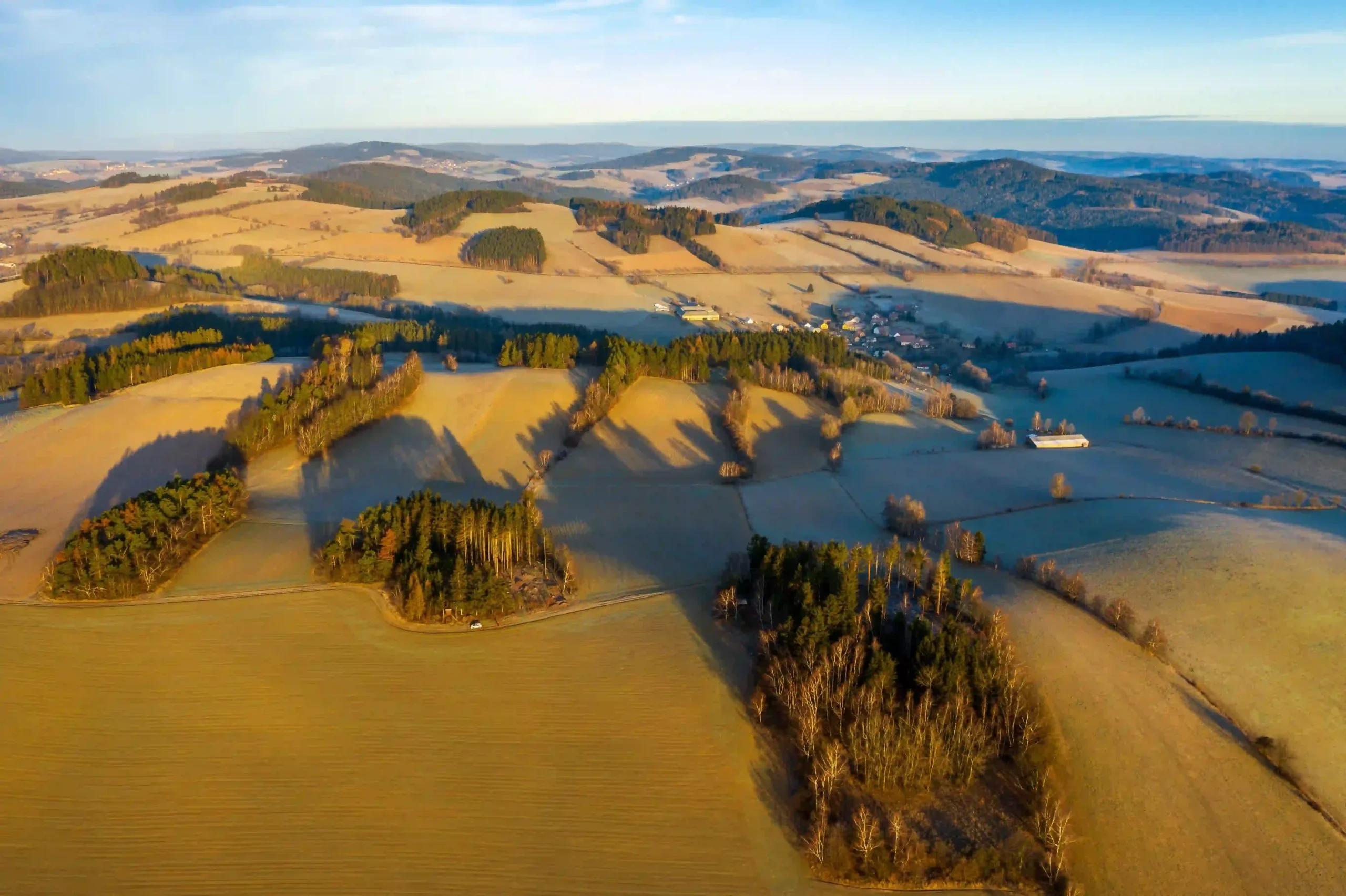 A serene aerial view of golden fields, small lakes, and scattered forests glowing in the sunset light.