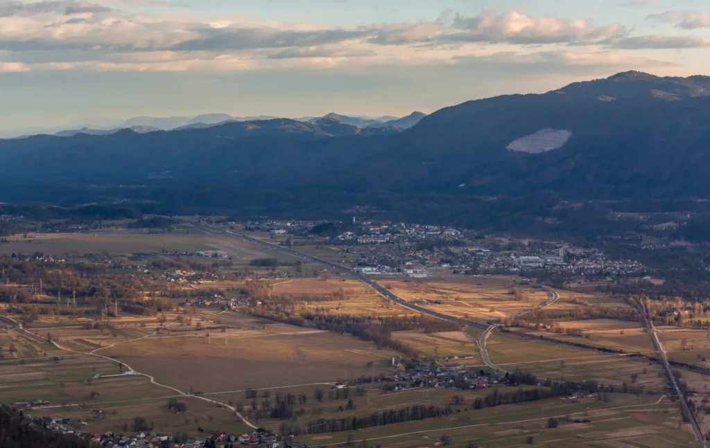 An aerial shot of a peaceful valley with fields and mountains under a partly cloudy sky.
