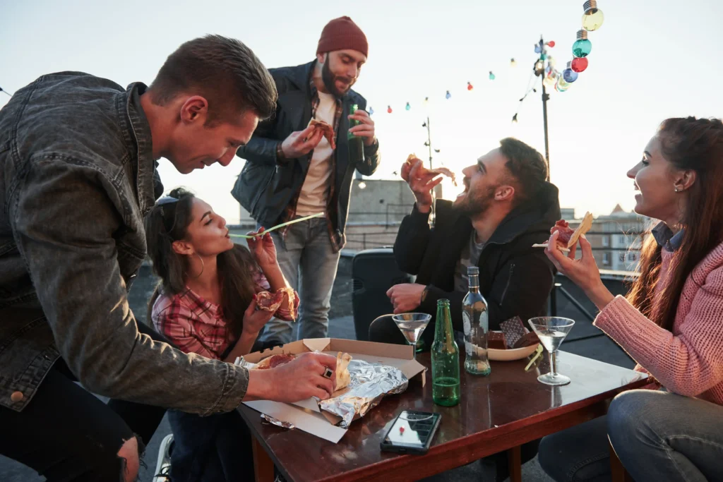 A group of friends enjoys food and drinks at a casual outdoor gathering.
