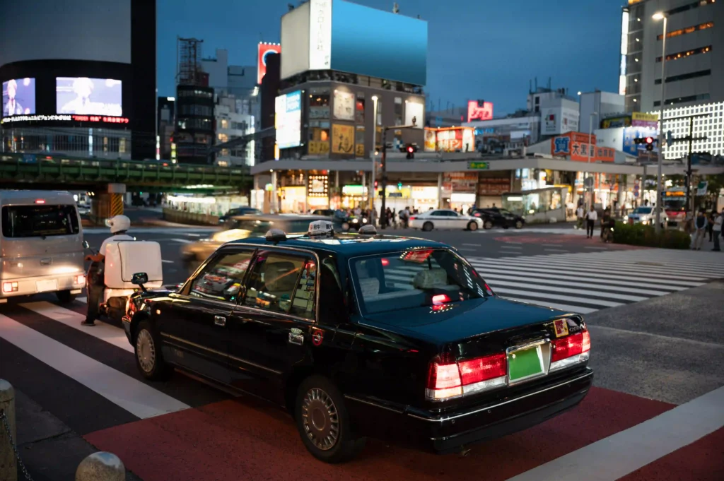 A vintage luxury car parked in a bustling city at night, under glowing lights.