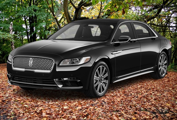 A black Lincoln Continental luxury sedan parked on a forest path covered with autumn leaves, surrounded by green and yellow foliage